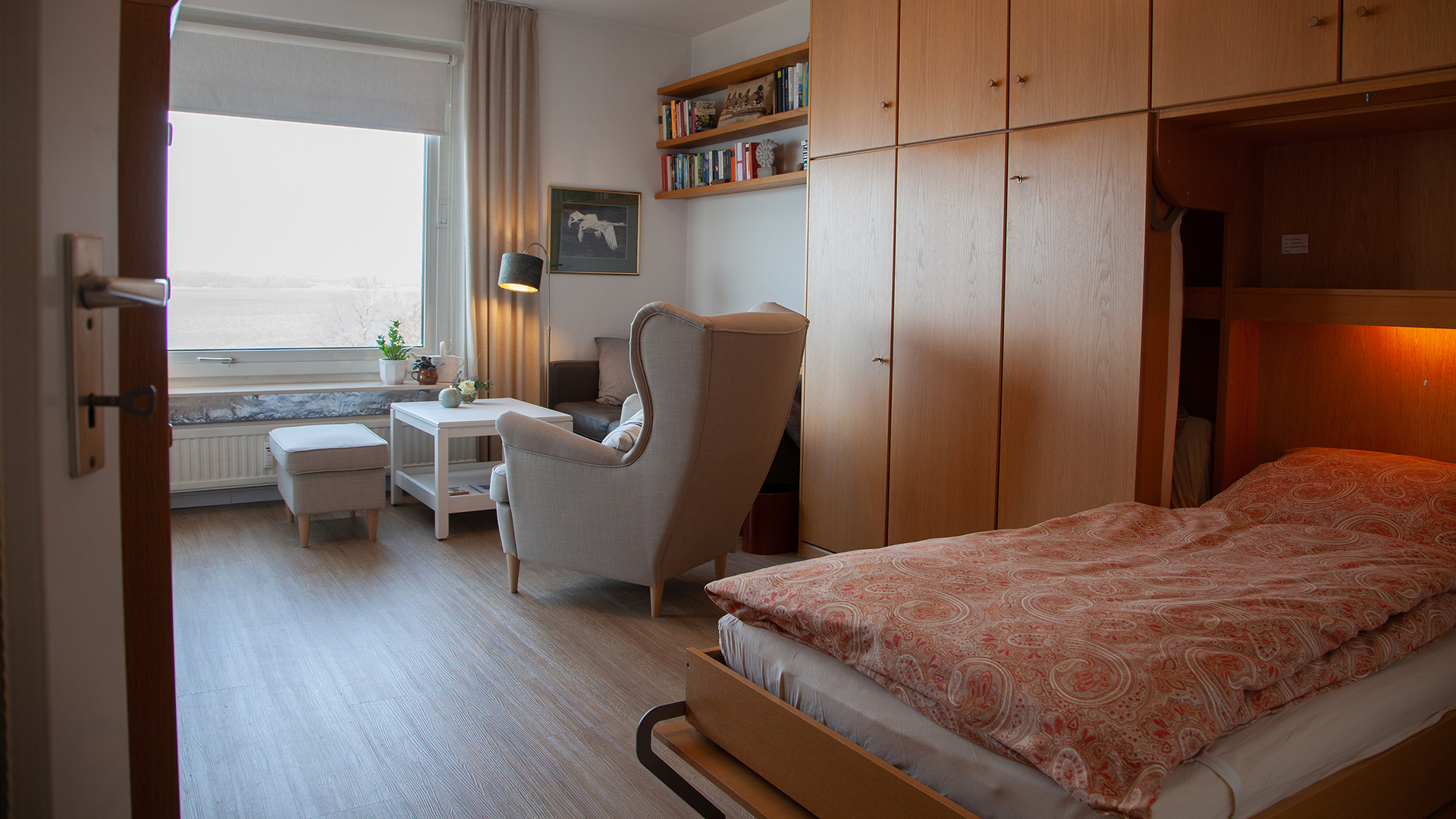 Ein Blick aus dem Flur in das erste Zimmer der Ferienwohnung Fiedler mit dem ausgeklappten Bett und der Wohnecke im Hintergrund.