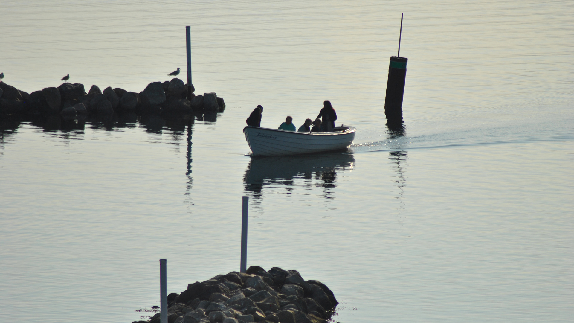 Ein kleines Holzboot mir 5 Personen fährt zwischen zwei Steinhaufen Richtung Land.
